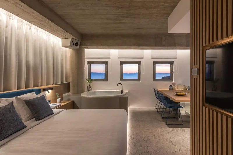 Chambre lumineuse avec un grand lit et une baignoire à remous face à la mer.
