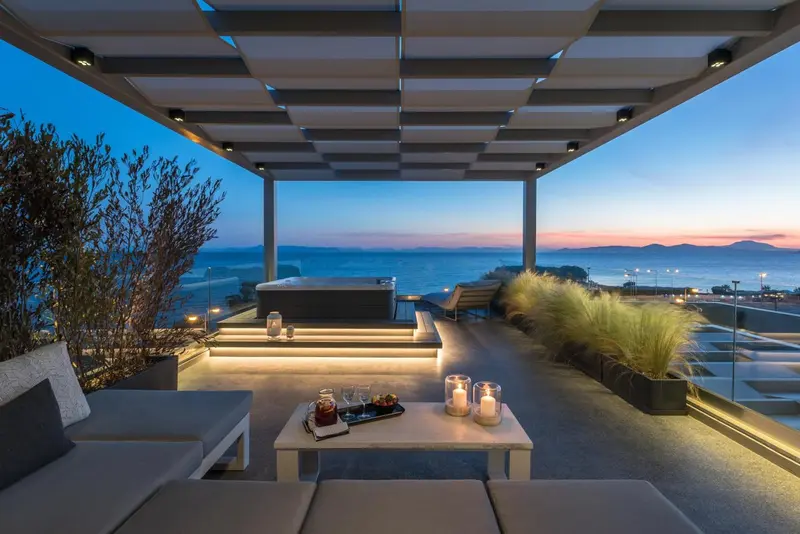 Terrasse aménagée avec salon et jacuzzi face à la mer au coucher du soleil.