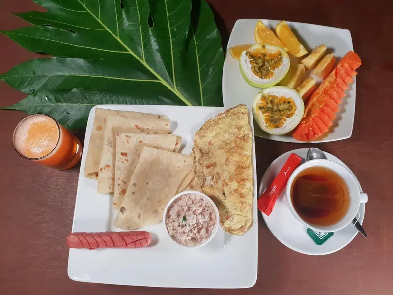 Un petit-déjeuner copieux est présenté sur une table blanche, avec des fruits frais et une boisson orangée.