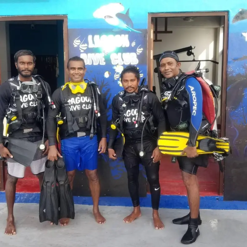 Quatre personnes en tenue de plongée posent devant un bâtiment.