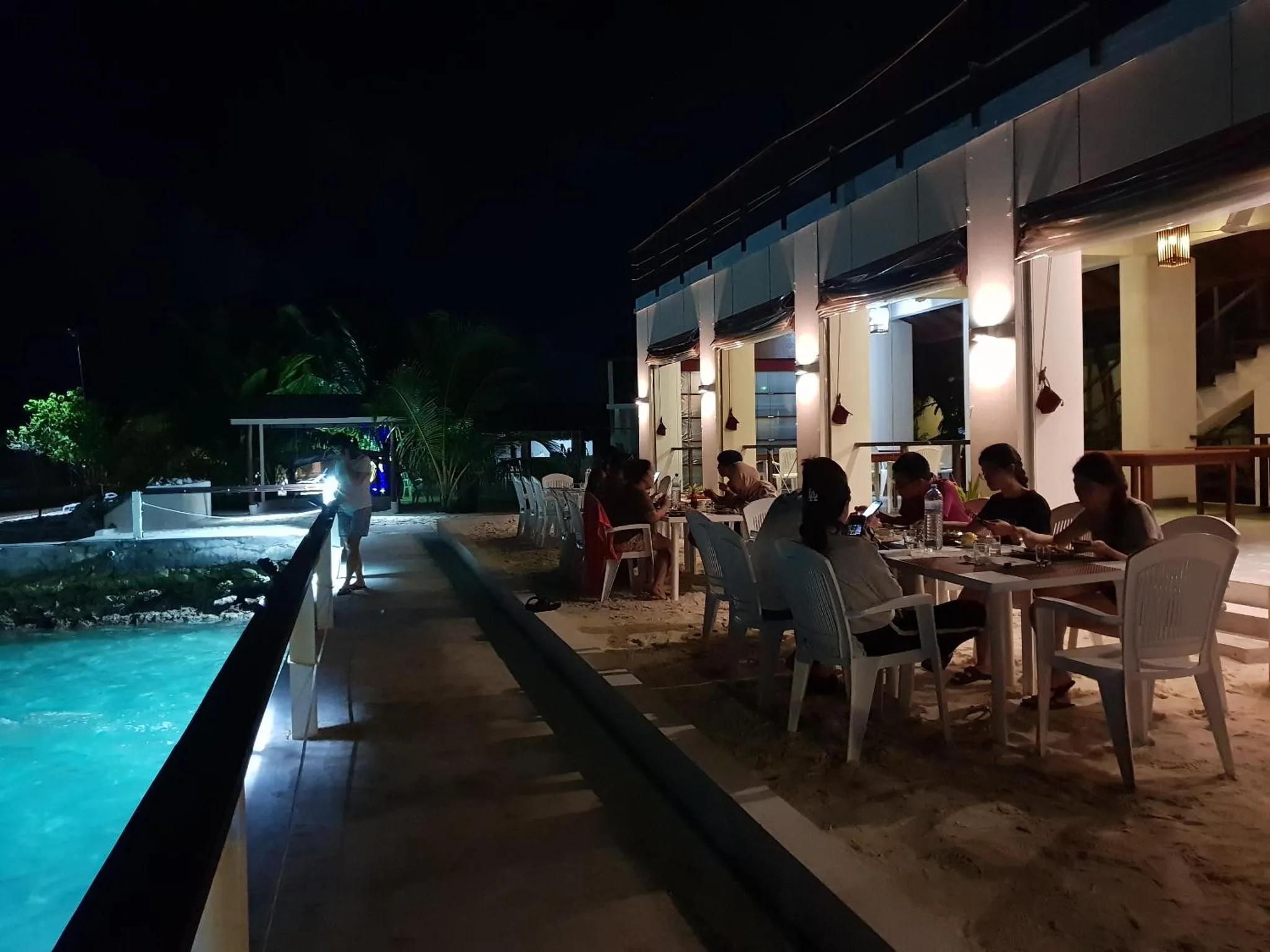 Des convives sont assis à des tables éclairées sur une terrasse en bord de mer.