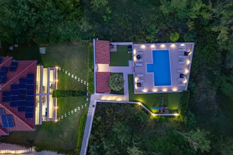 Vue aérienne d'une piscine rectangulaire et de bâtiments environnants éclairés.