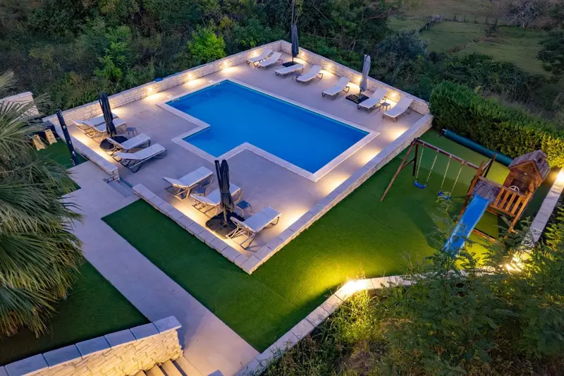 Vue aérienne d'une piscine rectangulaire entourée d'une terrasse et d'une pelouse.