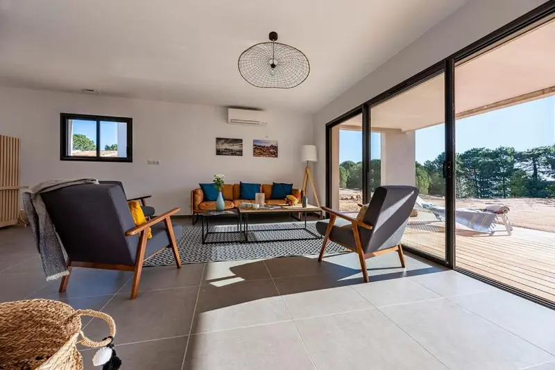 Un salon moderne avec canapés et fauteuils face à de grandes baies vitrées.