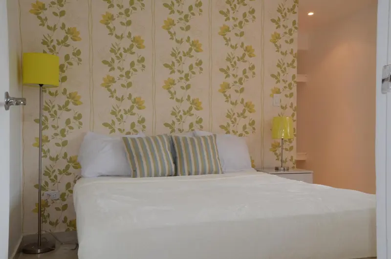 Une chambre lumineuse avec un lit recouvert d'une courtepointe blanche et de coussins.