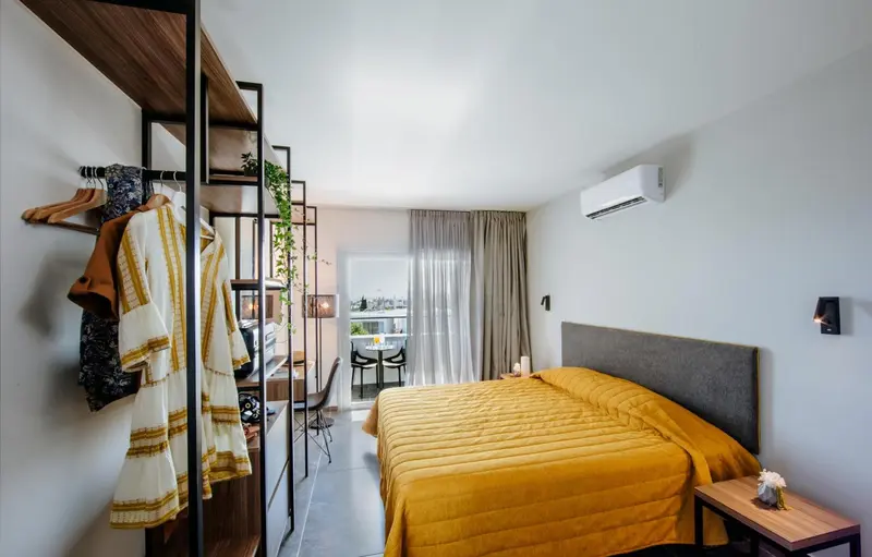 Une chambre lumineuse avec un lit recouvert d'une couverture jaune et un espace ouvert avec un portant à vêtements.