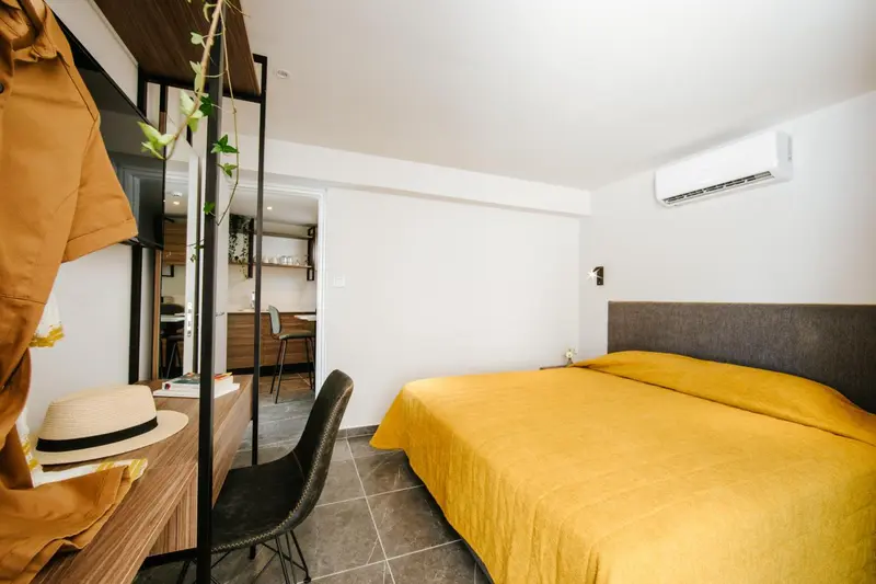 Une chambre lumineuse avec un lit recouvert d'un drap jaune et un bureau en bois.
