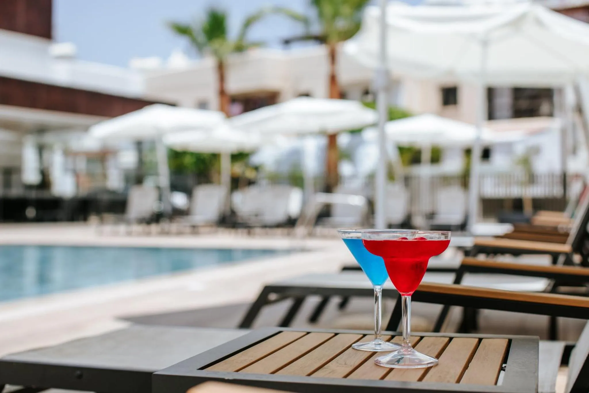 Deux cocktails colorés reposent sur une table basse au bord d'une piscine ensoleillée.