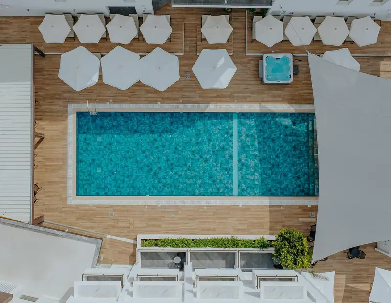 Vue aérienne d'une piscine rectangulaire entourée d'une terrasse en bois avec des transats blancs.
