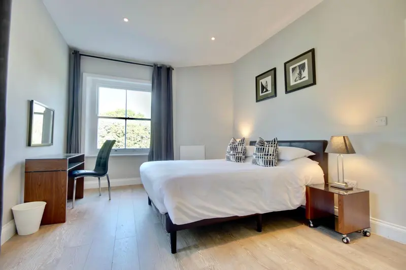 Une chambre lumineuse avec un lit double et un bureau près de la fenêtre.