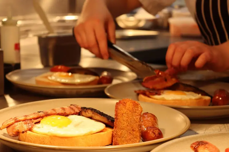 Des assiettes de petit-déjeuner avec des œufs, du bacon et des toasts sont préparées en cuisine.