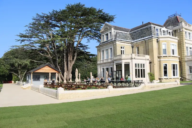 Bâtiment à l'architecture classique avec une terrasse ensoleillée et une pelouse verdoyante.