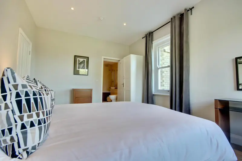 Une chambre lumineuse avec un lit fait et un accès à une salle de bain.