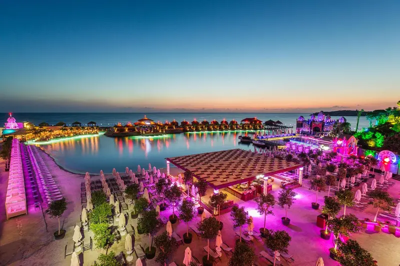 Vue aérienne d'un complexe hôtelier illuminé au crépuscule avec piscine et transats.