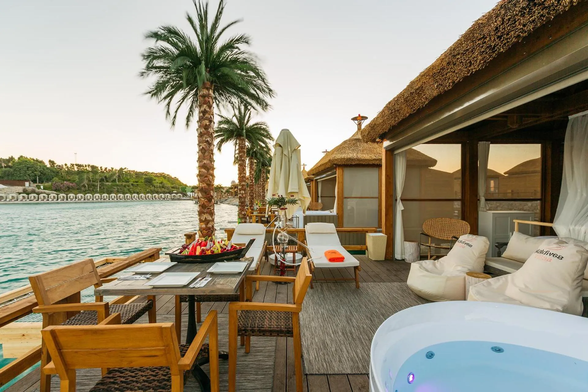 Terrasse en bois avec table, chaises et transats face à la mer.