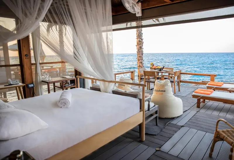 Lit recouvert de moustiquaire dans une chambre ouverte sur une terrasse avec vue sur la mer.