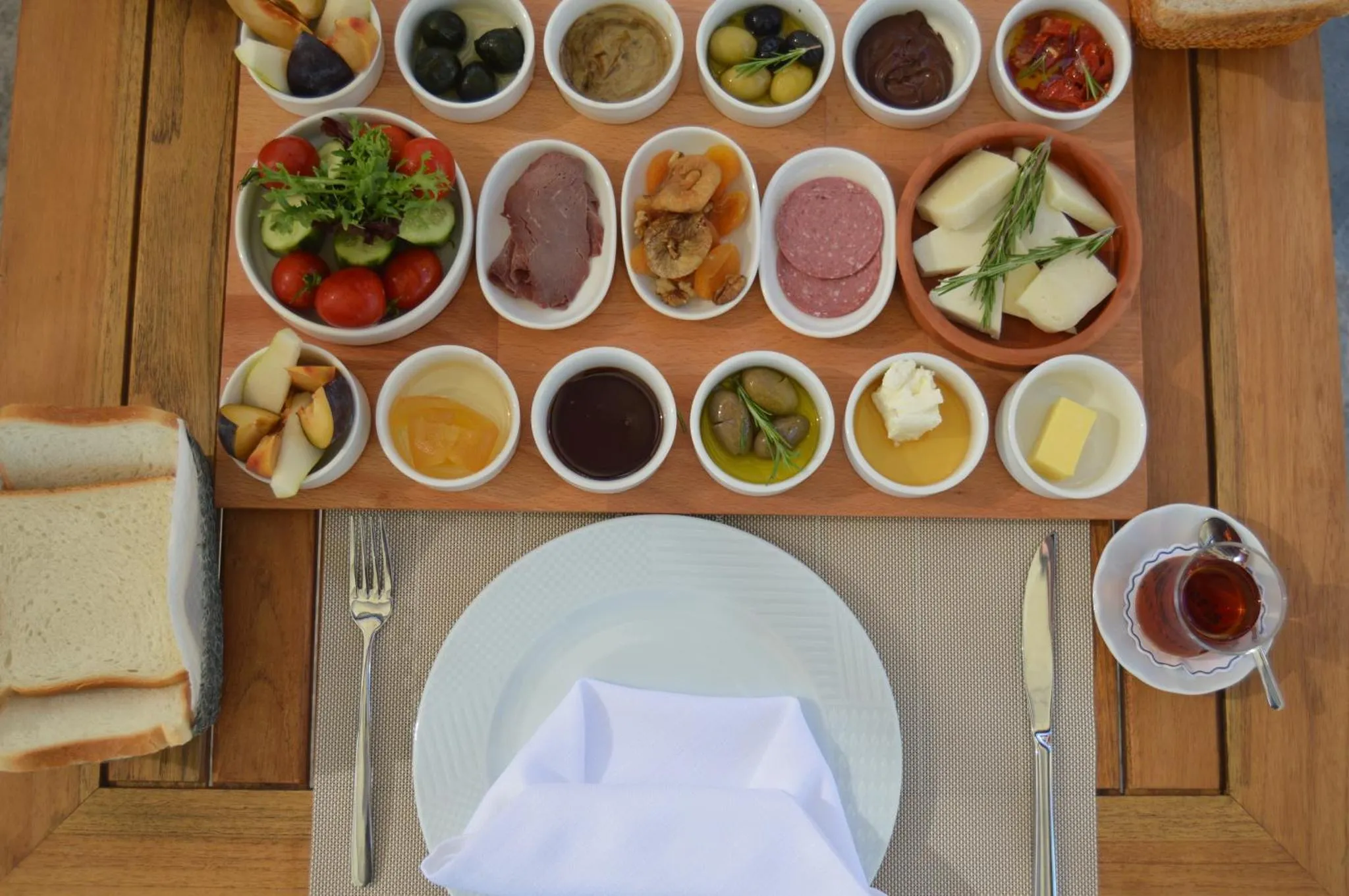 Assortiment de mets variés disposés sur une planche en bois, accompagnés de pain et de couverts.