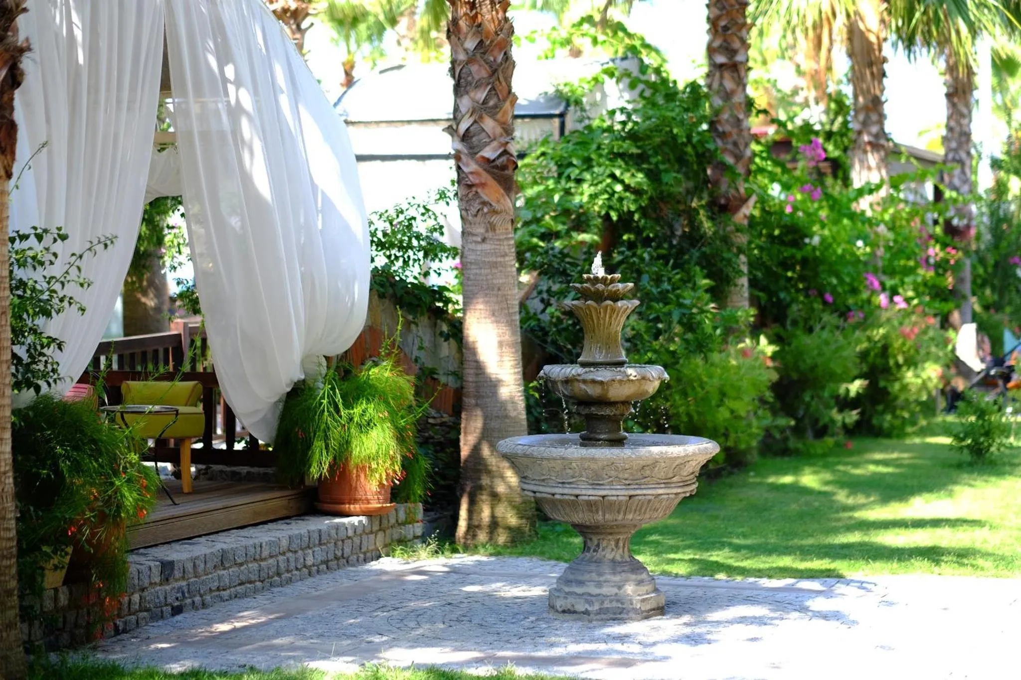Un jardin luxuriant avec une fontaine ornementale et un espace de détente ombragé.