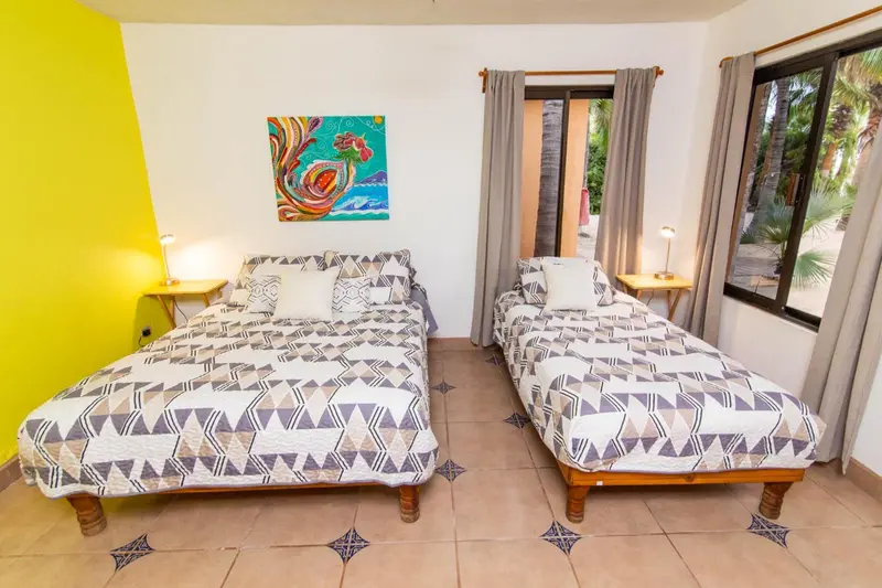 Une chambre lumineuse avec deux lits simples et une décoration murale colorée.