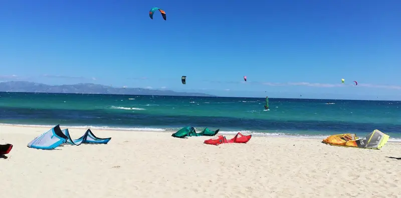 Une plage de sable clair avec des cerfs-volants colorés et une mer turquoise.