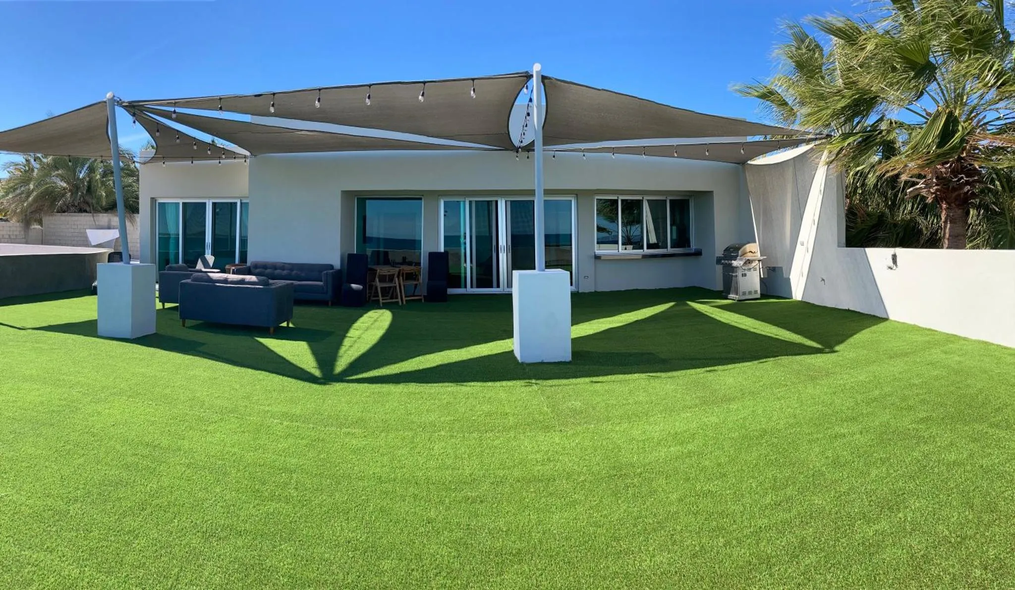 Terrasse ombragée avec mobilier de jardin et vue sur la mer.