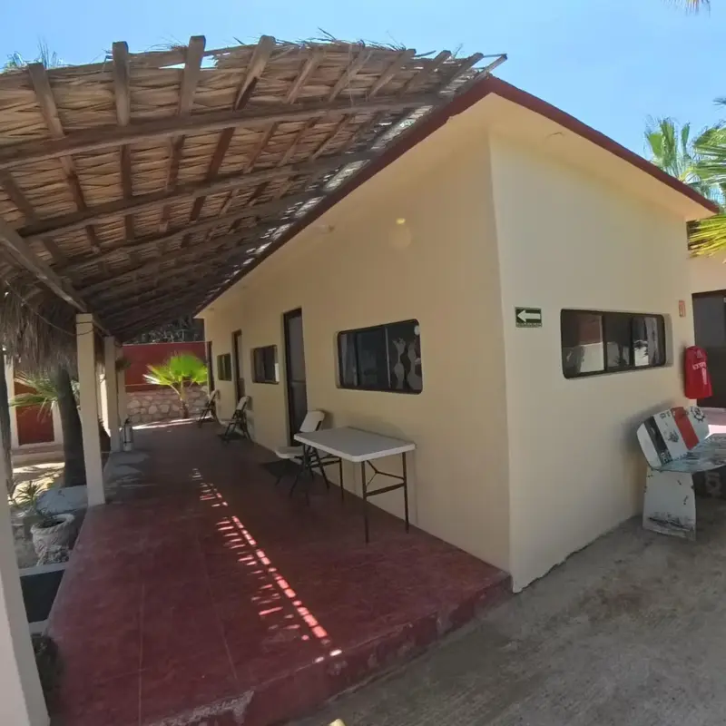 Bâtiment beige avec une terrasse ombragée et des tables.