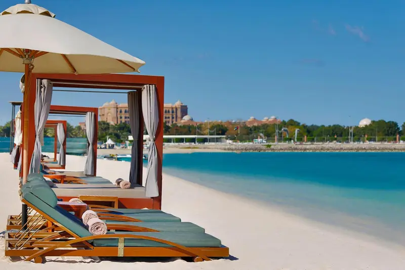 Transats et parasols sur une plage de sable blanc bordée d'une eau turquoise.