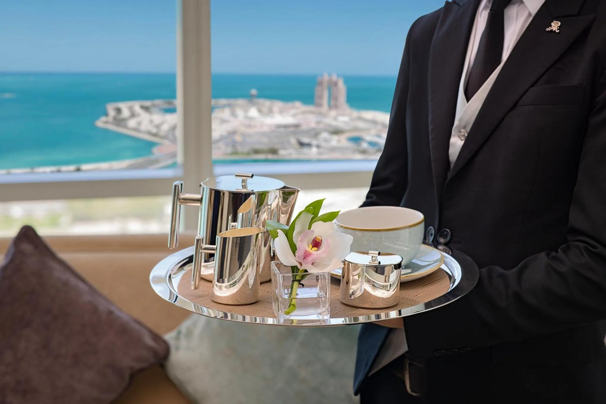 Un serveur présente un plateau avec une théière et une tasse sur fond de vue sur la mer.