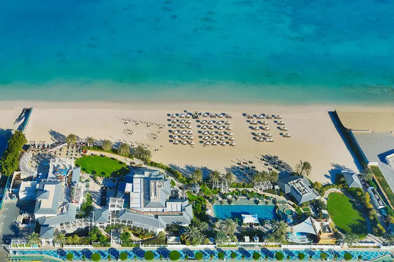 Vue aérienne d'une plage de sable fin bordée de transats et d'un complexe hôtelier.
