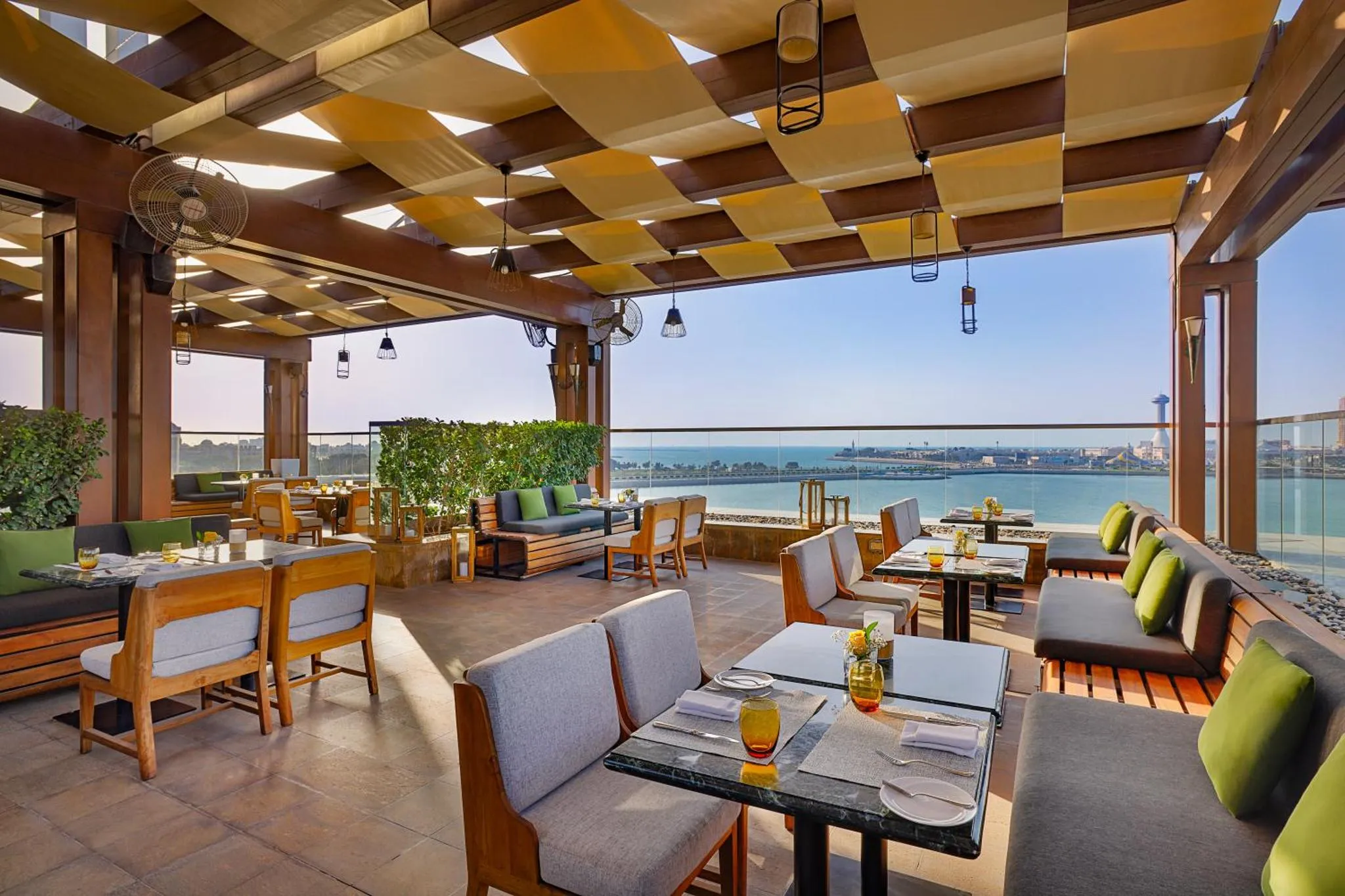 Une terrasse ombragée avec des tables et des chaises offre une vue sur la mer.