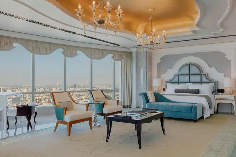 Une chambre lumineuse avec un grand lit et des fauteuils confortables offre une vue sur la ville.
