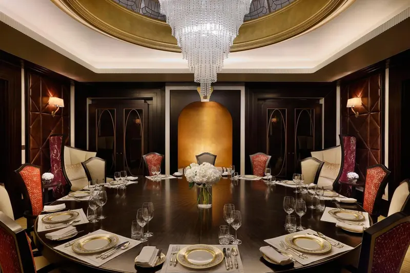 Une grande table ronde est dressée pour un repas dans une salle à manger élégante.