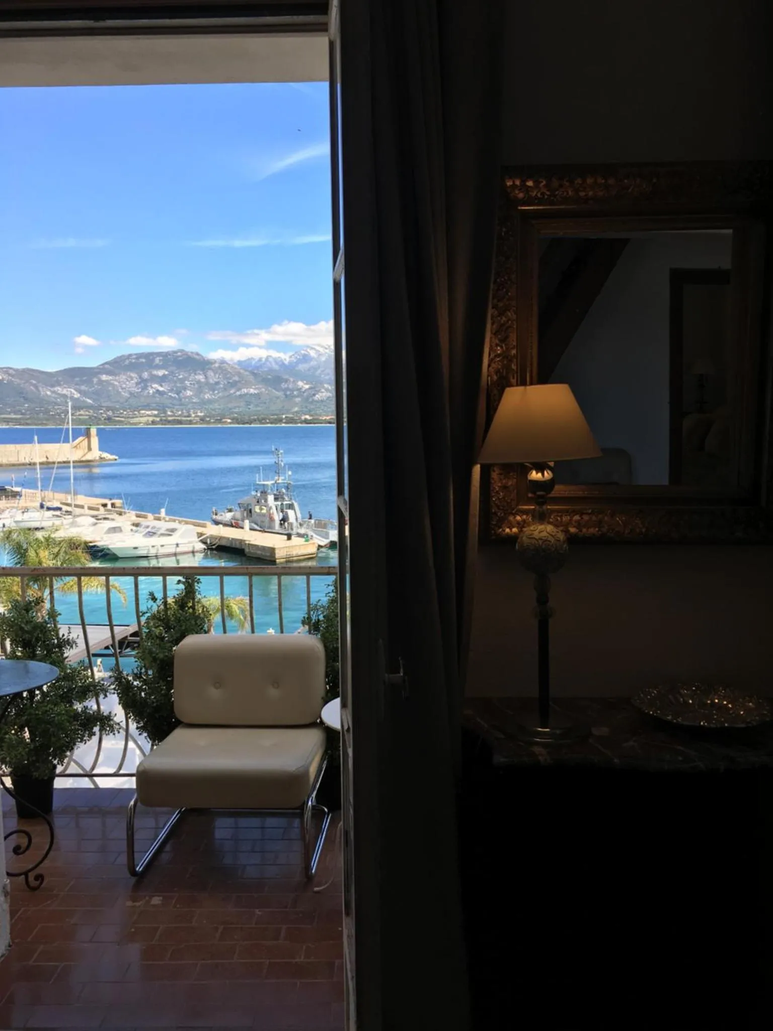 Une chaise est placée devant une fenêtre ouverte donnant sur la mer et les montagnes.