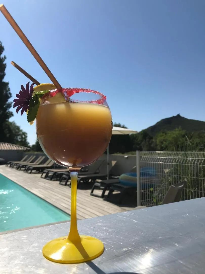 Un cocktail coloré est présenté sur une terrasse ensoleillée avec vue sur une piscine.