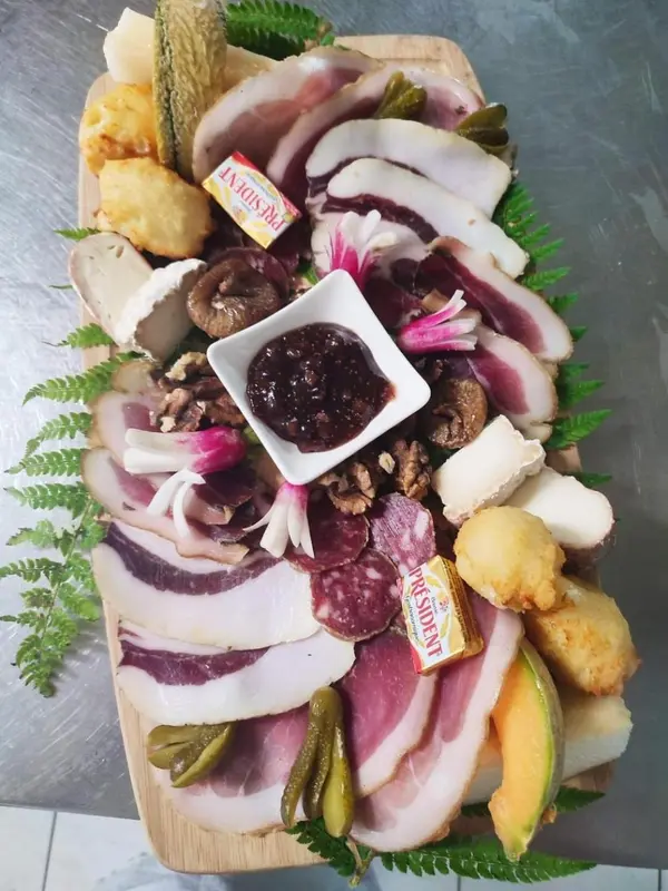 Assortiment de charcuteries, fromages et cornichons présentés sur une planche en bois.