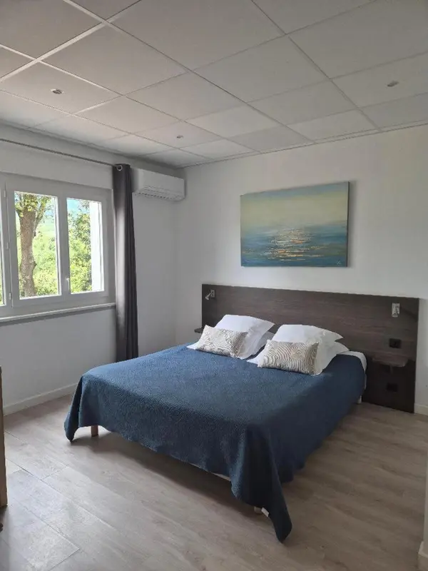 Une chambre lumineuse avec un lit fait et un tableau abstrait au mur.
