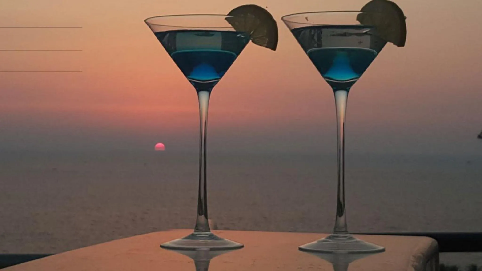 Deux cocktails bleus sont servis sur une table face à la mer au coucher du soleil.