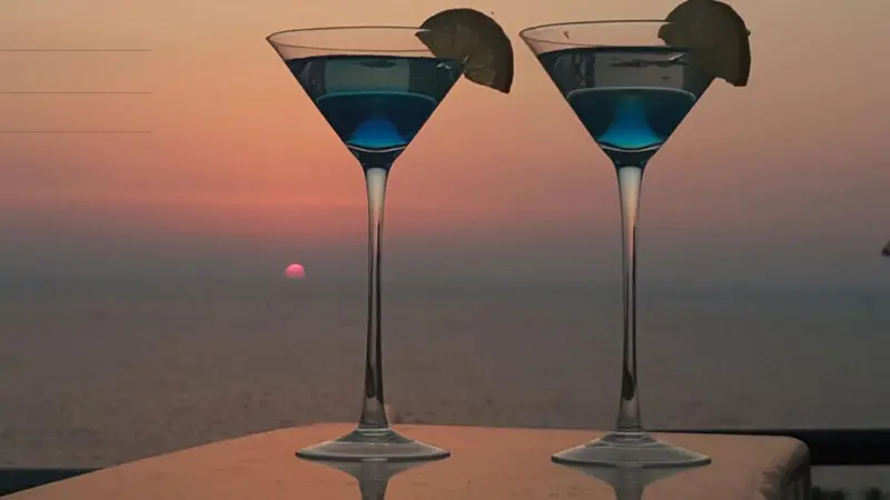 Deux cocktails bleus sont servis sur une table face à la mer au coucher du soleil.