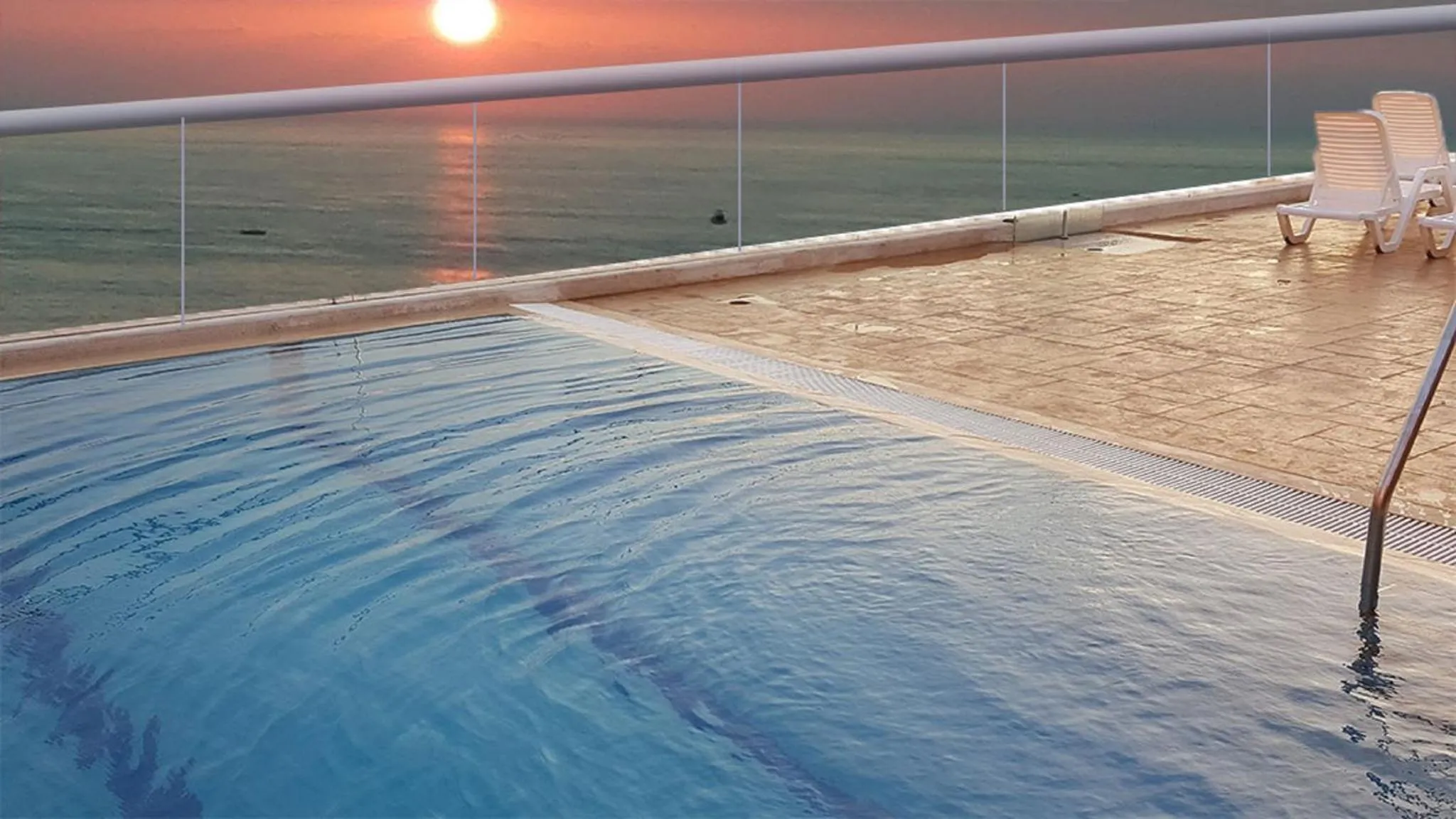 Piscine à débordement avec vue sur la mer au coucher du soleil.