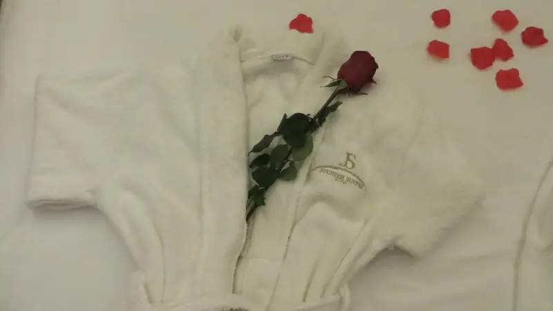 Un peignoir blanc et une rose rouge reposent sur un lit.