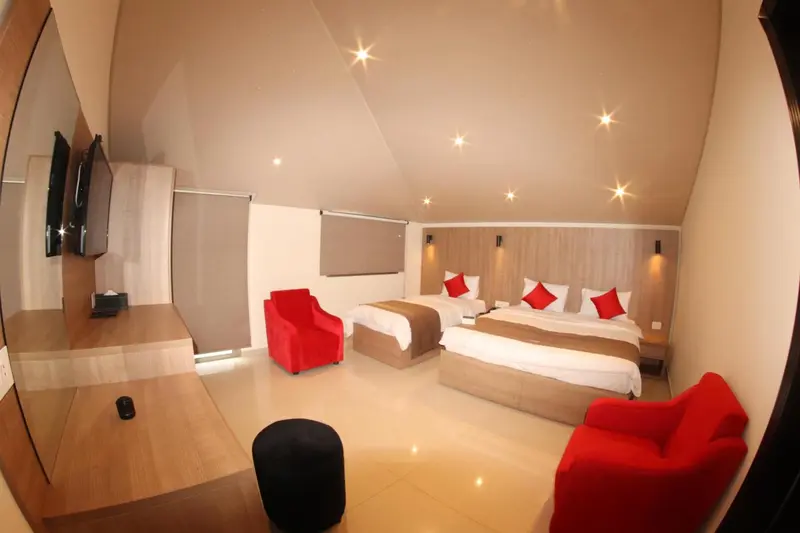 Chambre lumineuse avec deux lits et des fauteuils rouges.