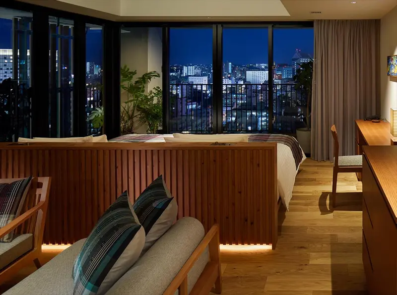 Une chambre avec un grand lit et un coin salon donnant sur une vue nocturne de la ville.