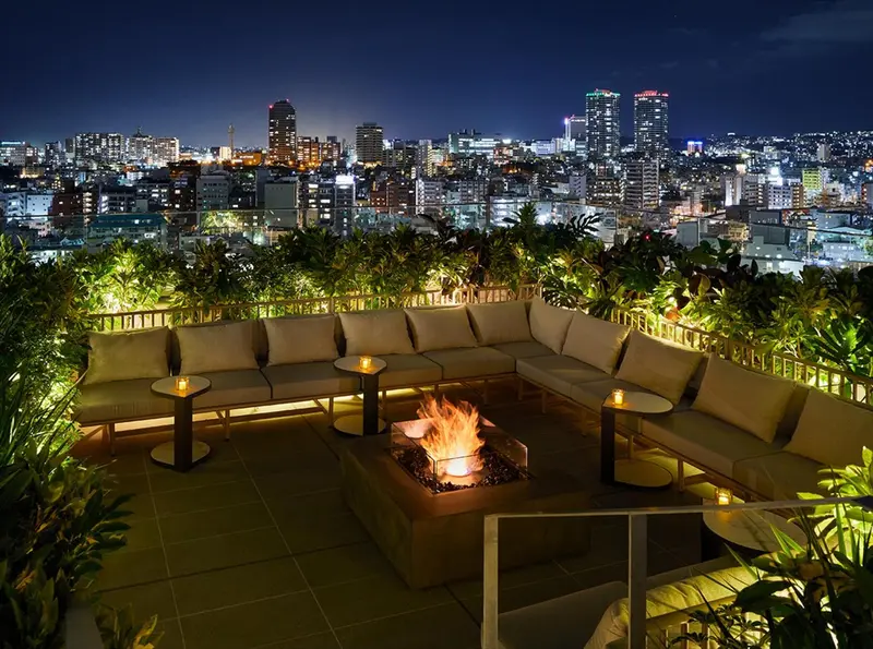 Terrasse aménagée avec des canapés et un foyer extérieur, donnant sur une ville illuminée.