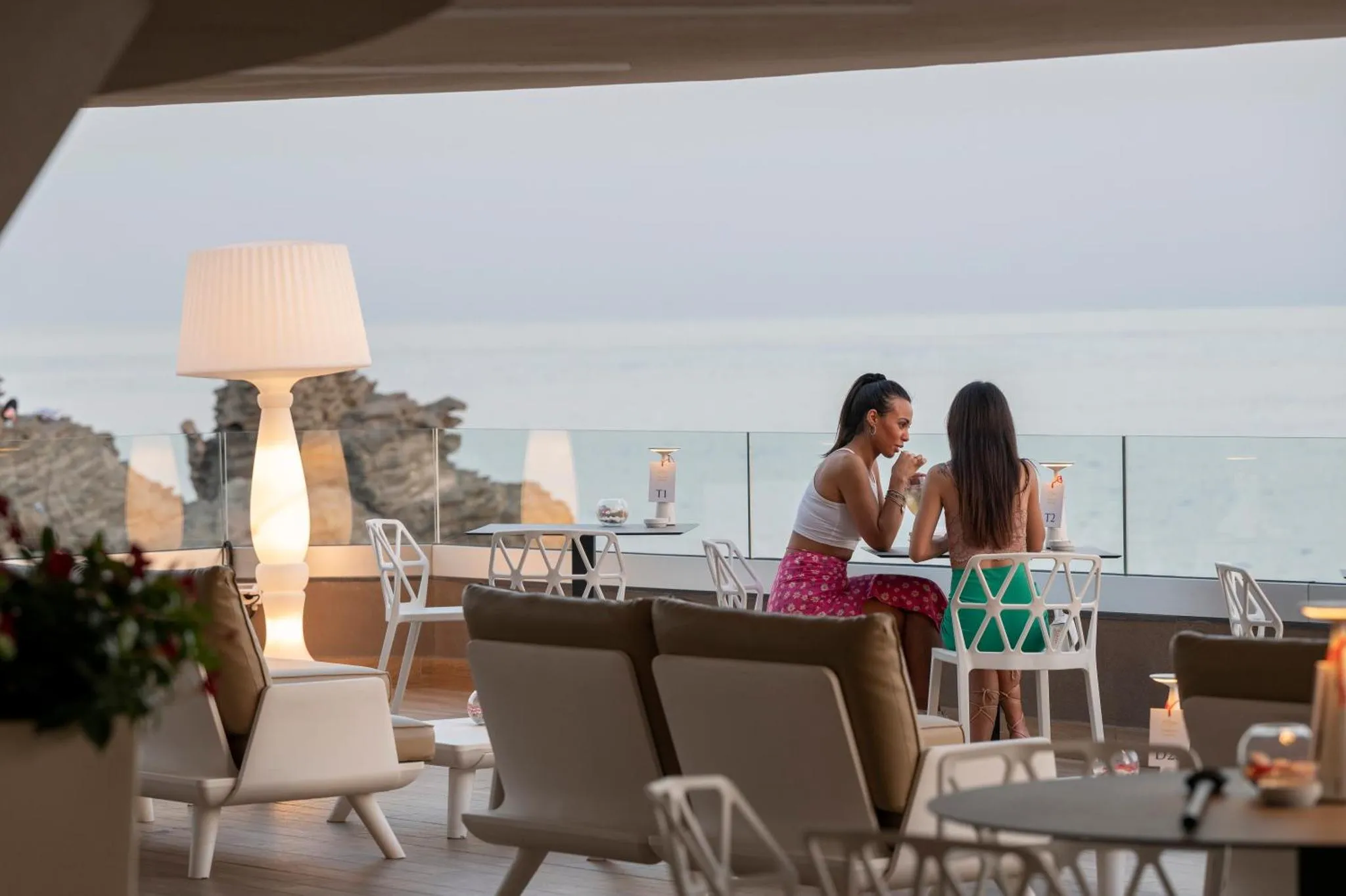Deux personnes sont assises à une table sur une terrasse avec vue sur la mer.