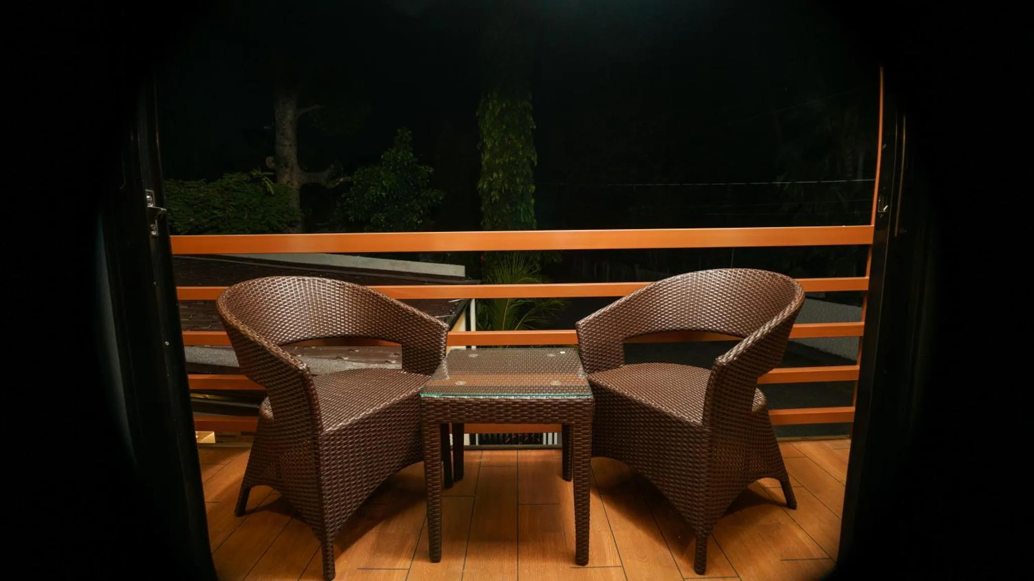 Deux fauteuils en osier et une petite table sur une terrasse sombre.