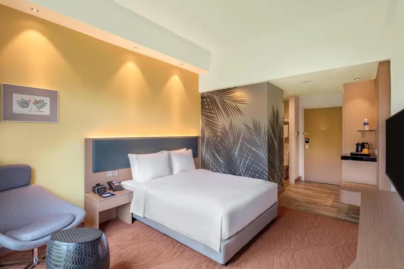 Une chambre d'hôtel lumineuse avec un grand lit et un fauteuil.