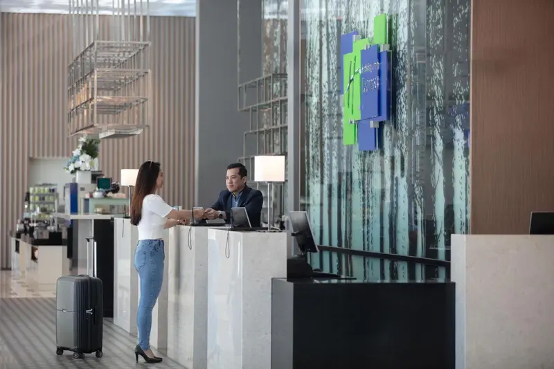 Une réception d'hôtel moderne avec deux employés et une cliente.