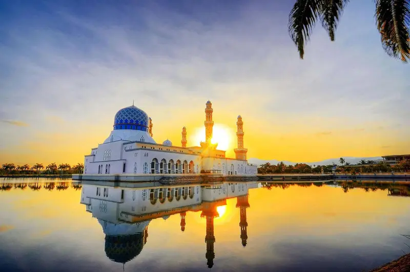 Une mosquée blanche se reflète dans l'eau au coucher du soleil.