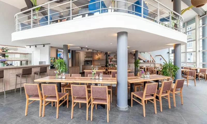 Une grande salle lumineuse avec un bar et des tables à manger en bois.
