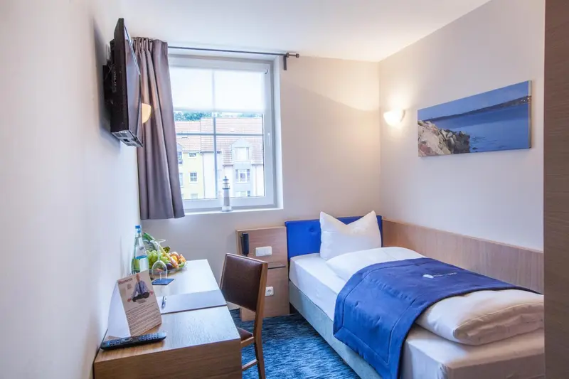 Une chambre simple avec un lit et un bureau près d'une fenêtre.